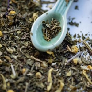 Detailed view of dried herbal tea leaves scattered with a ceramic spoon.
