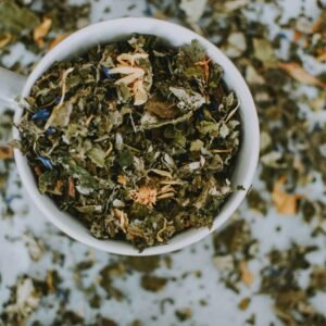 Overhead shot of a cup with a blend of dried herbal tea leaves and flowers.